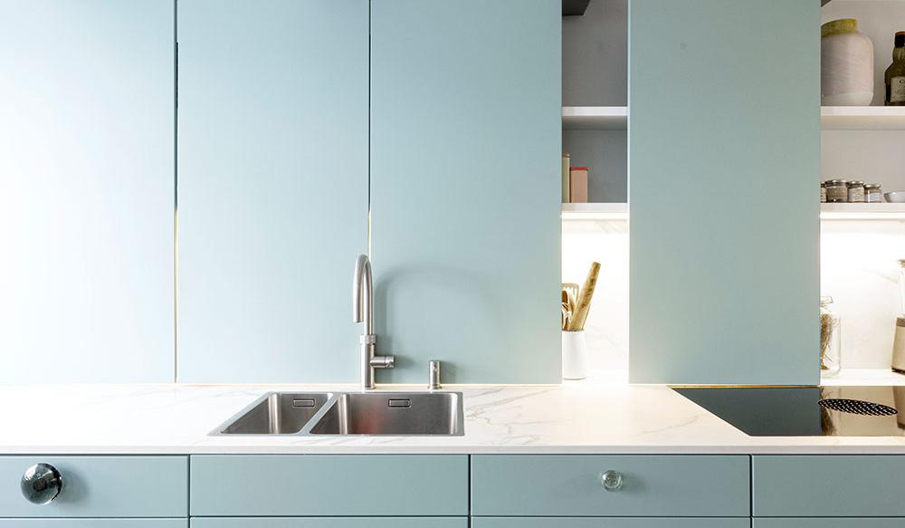 Moderne Küche mit hellblauen Schränken, weißer Arbeitsplatte und Edelstahlspüle.