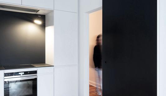 Moderne weiße Küche mit schwarzer Schiebetür und Holzfußboden.