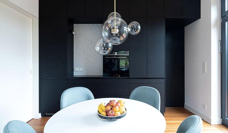 Runder Tisch mit Obstschale, moderne schwarze Küchenzeile im Hintergrund.