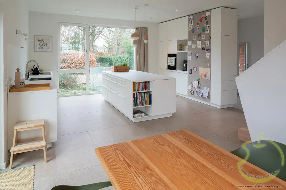 Helle, moderne Küche mit Kochinsel, Esstisch und großem Fenster zum Garten.