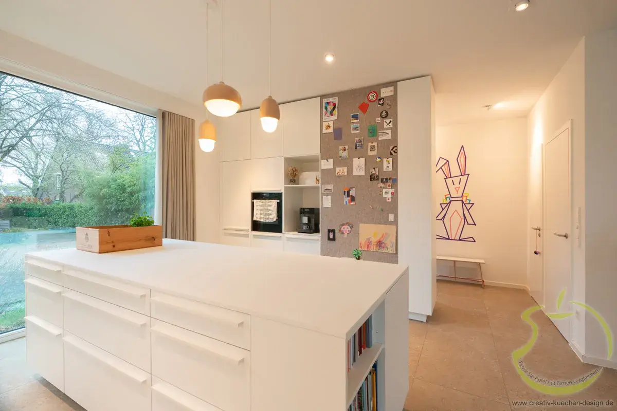 Moderne, helle Küche mit großem Fenster, weißer Insel und bunter Wanddekoration.