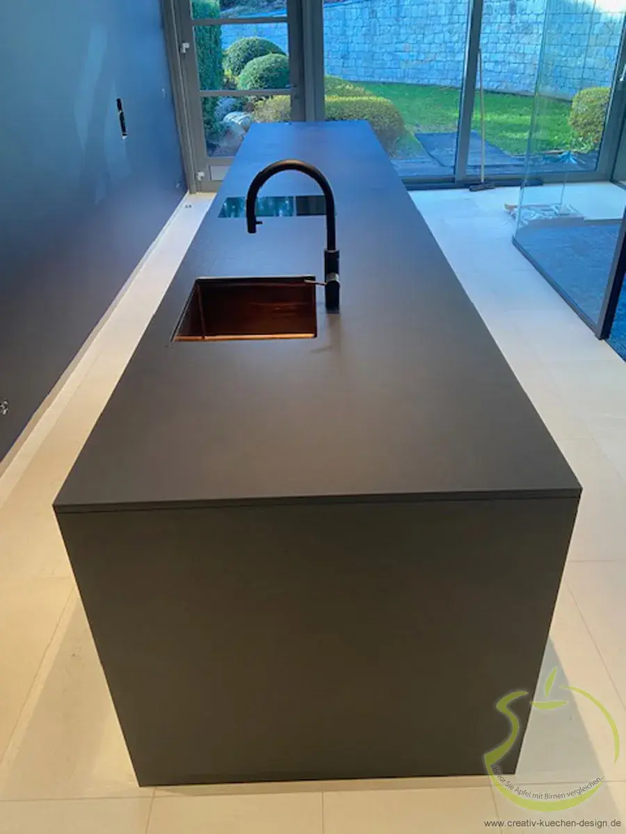 Moderne schwarze Kücheninsel mit Spüle und Wasserhahn, große Fenster im Hintergrund.