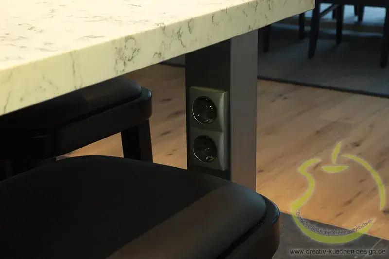 Steckdosen an Tischbein, Stuhl und Holzboden im modernen Raum.