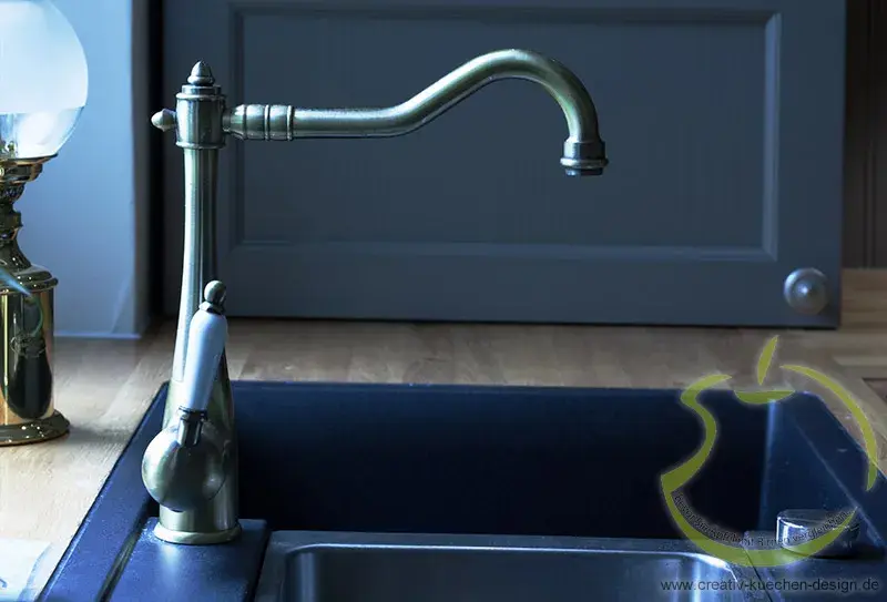 Messingfarbene Küchenarmatur über schwarzem Spülbecken vor einer blauen Tür.