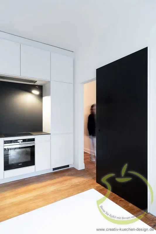 Moderne weiße Küche mit schwarzer Schiebetür und Holzfußboden.