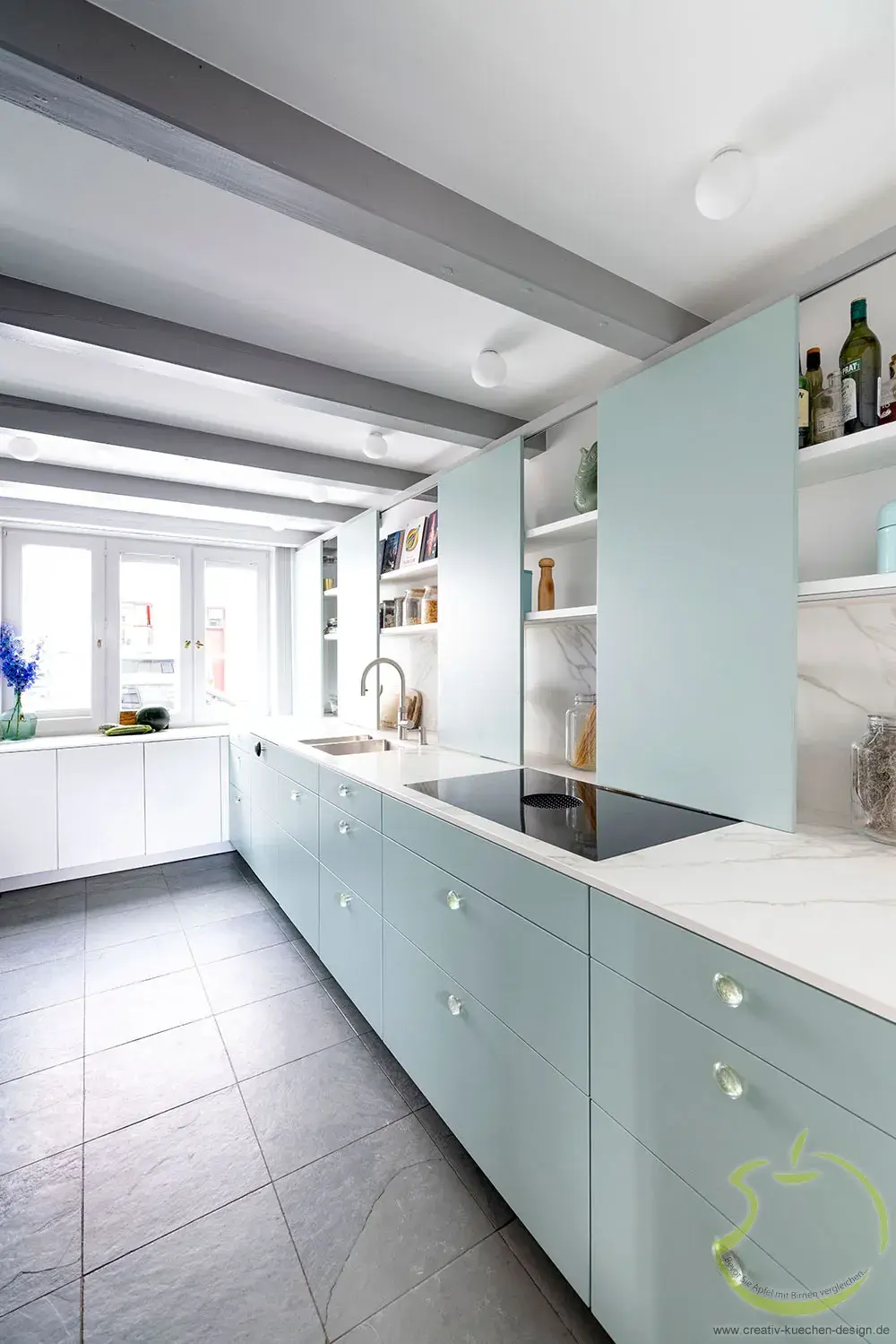 Moderne Küche mit hellblauen Schränken, weißen Arbeitsplatten und großen Fenstern.