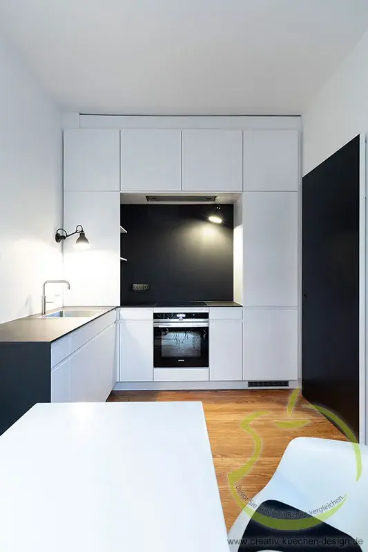 Moderne weiße Einbauküche mit schwarzem Herd und Holzfußboden.