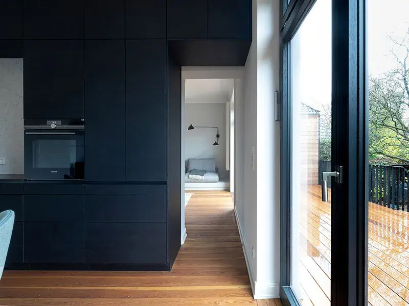 Modernes, helles Wohnzimmer mit Holzboden, dunkler Küche und großer Glas-Schiebetür.
