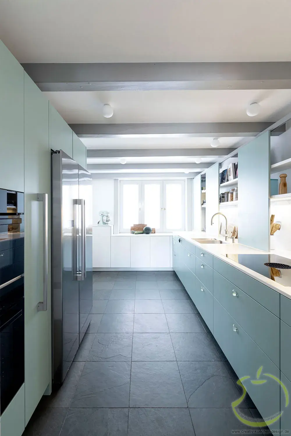 Moderne Küche mit hellblauen Schränken, großem Fenster und grauem Fliesenboden.