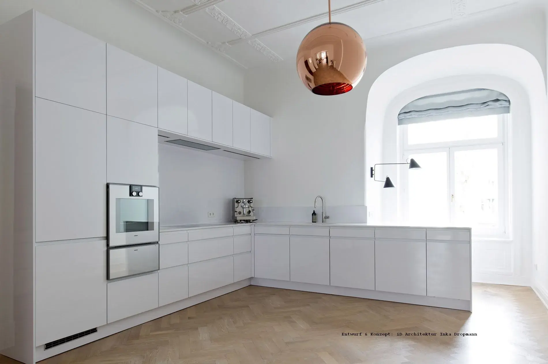 Moderne, helle Küche mit weißen Hochglanzschränken und Kupferlampe.